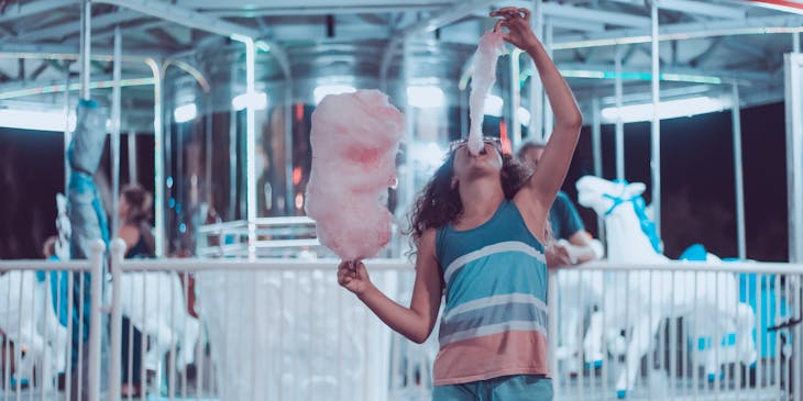 A young girl eating cotton candy at a fair.