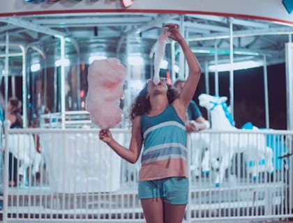 Une jeune fille mange de la barbe à papa à une fête foraine.