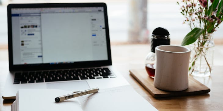 Open notebook with a pen in front of an open laptop, ready to be creative.