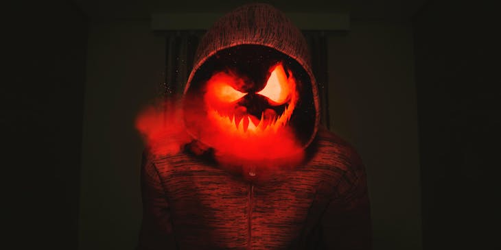 A creepy glowing pumpkin face in a red hoodie.