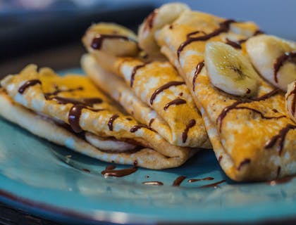 Una crepa con plátano y chocolate sobre un plato azul en una crepería.