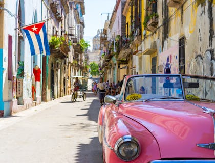 Una tipica via di Cuba con un'automobile vintage rossa parcheggiata e una bandiera cubana.