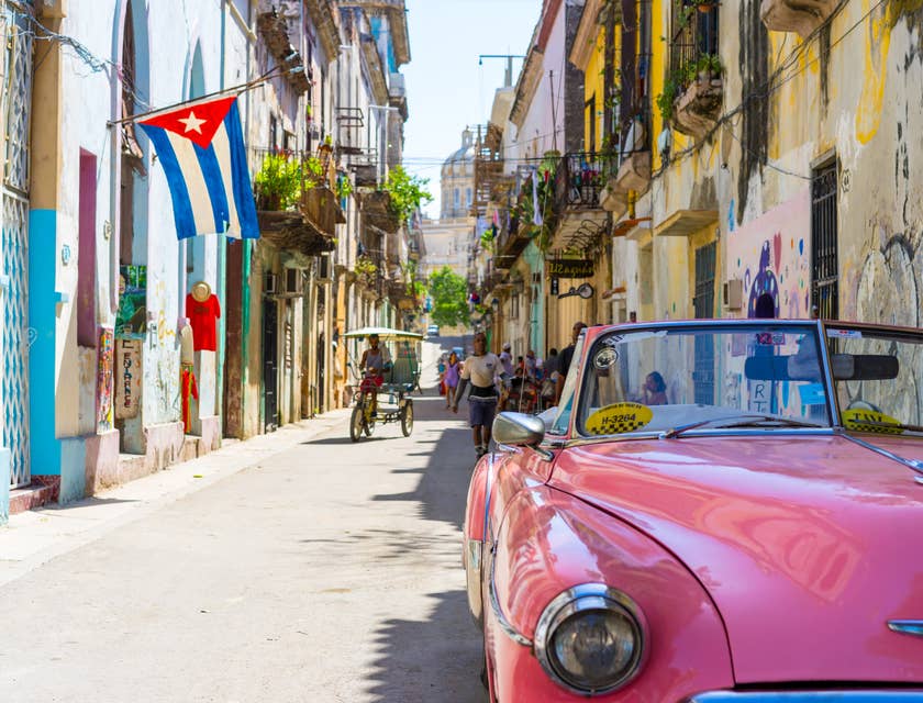 Una tipica via di Cuba con un'automobile vintage rossa parcheggiata e una bandiera cubana.