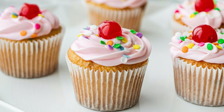 Pink cupcakes with sprinkles and red cherries on top.