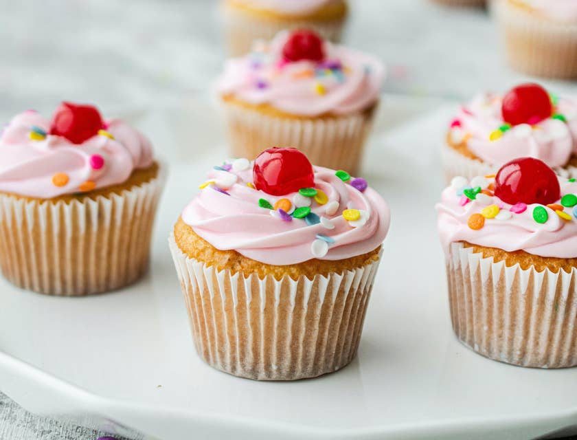 Pink cupcakes with sprinkles and red cherries on top.