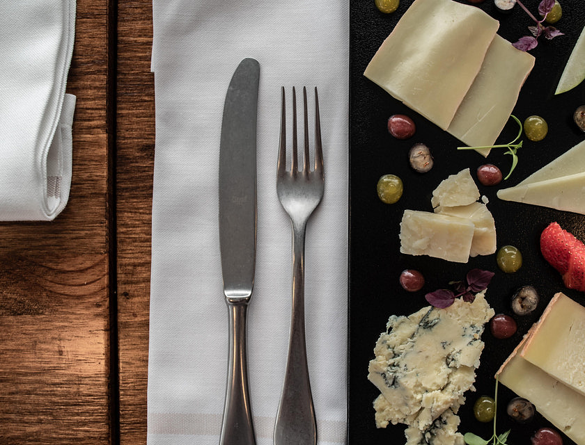 Cubiertos colocados sobre una servilleta de lino blanco sobre una mesa entre un plato con una variedad de quesos en un negocio de cubertería.