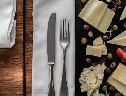Couverts, y compris un couteau et une fourchette, placés sur une serviette en lin blanc sur une table entre une assiette avec un assortiment de fromages.