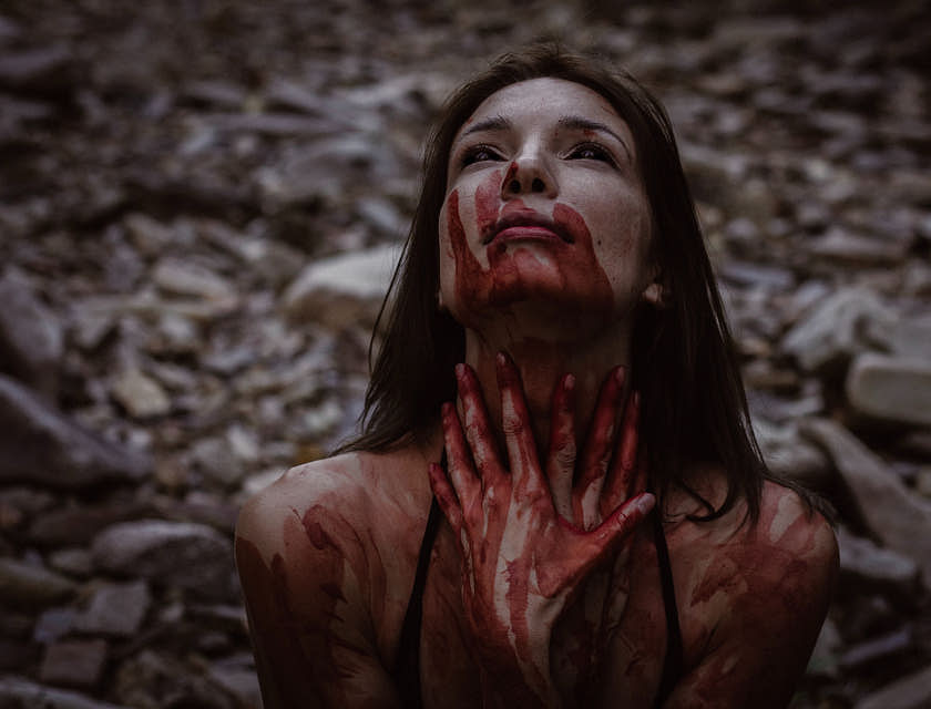 Una donna con le mani insanguinate sul collo in una scena dark.