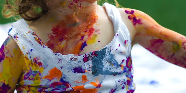 A delighted child covered in paint with a ribbon in her hair.