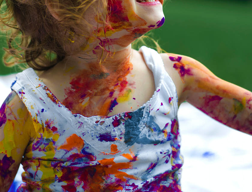 A delighted child covered in paint with a ribbon in her hair.