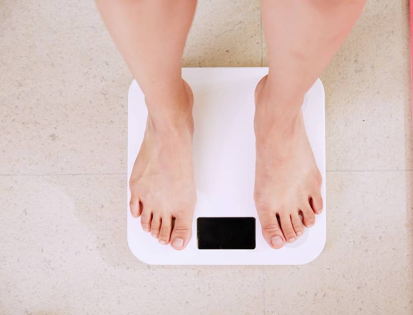 Pessoa de pé em uma balança branca no consultório de um profissional especializado em nutrição e dietética.