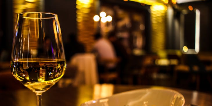 Glass of white wine next to a white bowl in a dimly lit dinner theater restaurant.