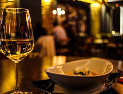 Glass of white wine next to a white bowl in a dimly lit dinner theater restaurant.