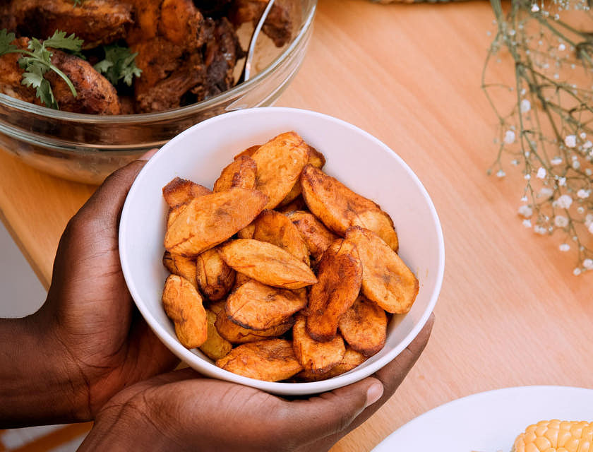 Las manos de una persona sosteniendo un bowl con plátanos fritos en un restaurante dominicano.