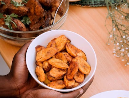 Las manos de una persona sosteniendo un bowl con plátanos fritos en un restaurante dominicano.