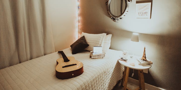 White on white bedroom with single bed, side table, lights, and a mirror above the bed.