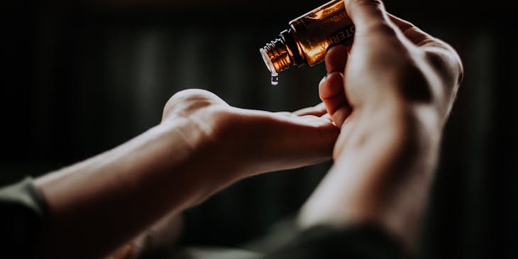 A hand tipping an essential oil bottle and dripping drops of oil into the other hand's palm.
