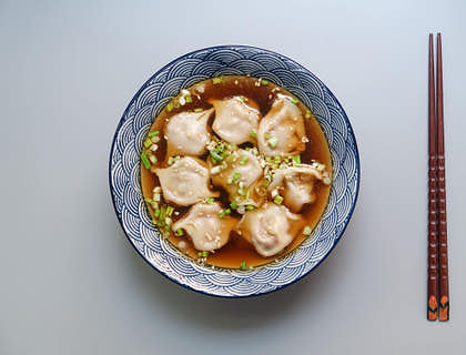 Raviolis asiatiques dans un bouillon servi dans un bol en céramique.