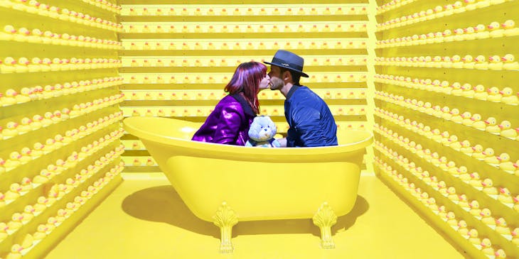 Two people kissing in an edgy yellow bathtub surrounded by yellow rubber ducks