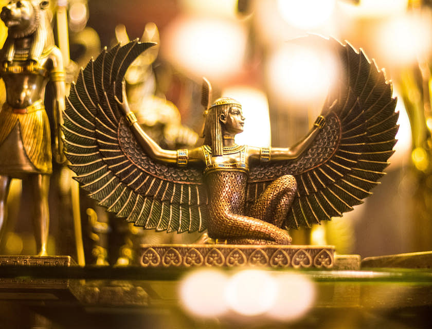 Estatueta da deusa egípcia com asas de ouro ajoelhada com as asas abertas.