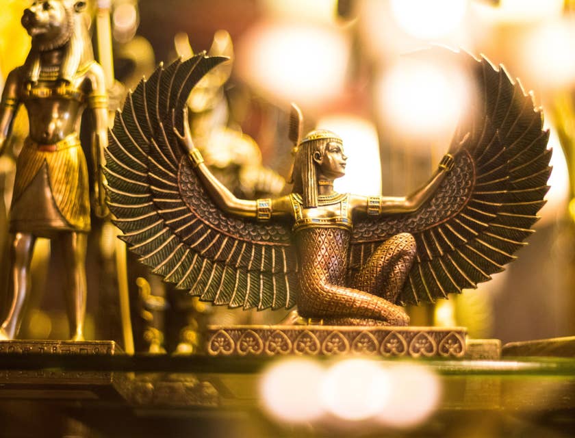 Figura de una diosa egipcia con alas doradas y extendidas arrodillada en negocio con nombre egipcio.