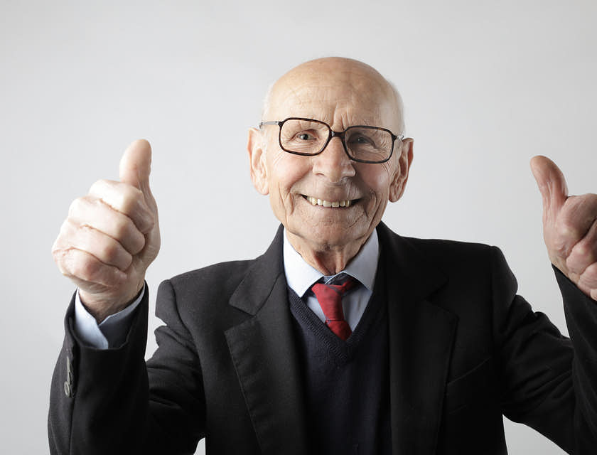 Elderly man in a black suit giving thumbs up signs with both hands.
