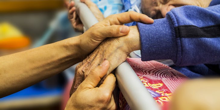 Holding the hand of an elderly man requiring eldercare planning services.