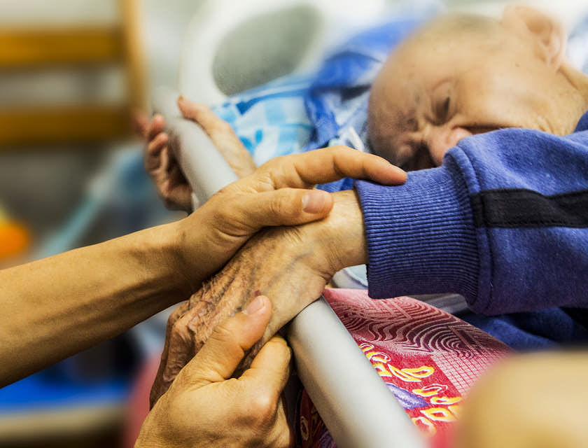 Holding the hand of an elderly man requiring eldercare planning services.