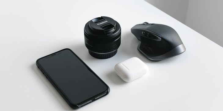 Black smartphone, camera lens, and wireless mouse arranged on a white surface.