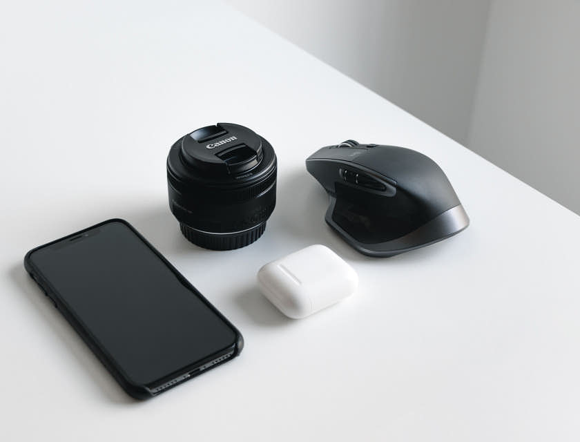 Un smartphone noir, objectif d'appareil photo et souris sans fil disposés sur une surface blanche.
