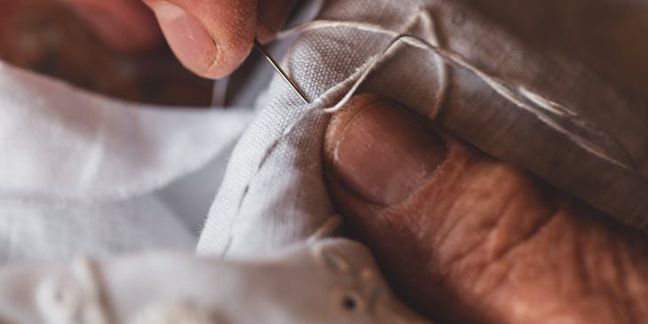 An embroiderer stitches with a needle.