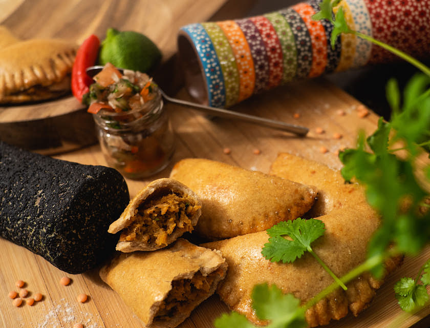 Empanadas liegen neben Salsa und Koriander auf einem Holzbrett.