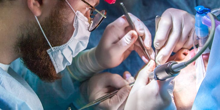 Two endodontists wearing scrubs while performing dental work on a patient.