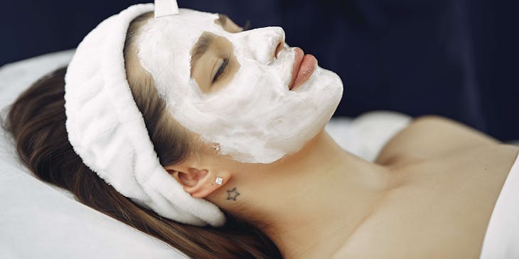 Esthetician putting a white face mask on a client.