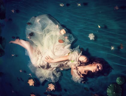 A woman wearing a white dress and posing against an ethereal background.