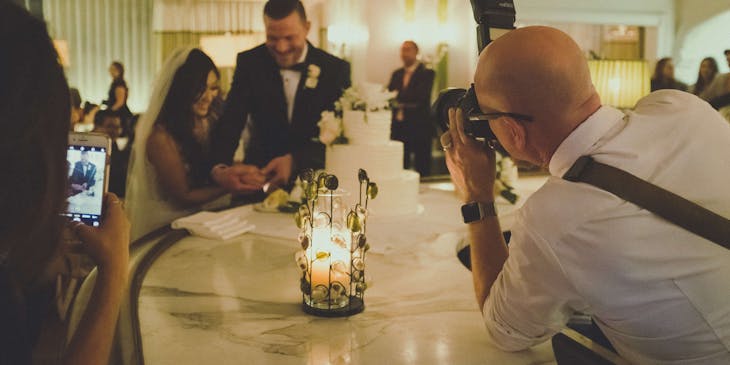 An event photographer taking a picture of the bride and groom slicing the cake.