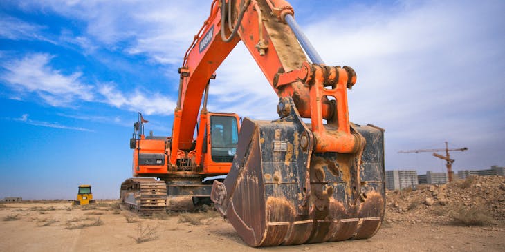 An orange excavator performing excavation services on a construction site.