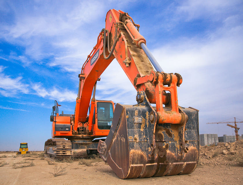 An orange excavator performing excavation services on a construction site.