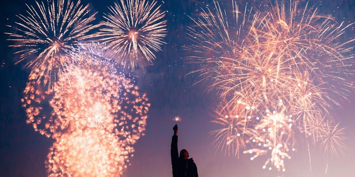 A man holding a sparkler in front of explosive fireworks .