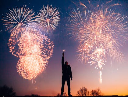 Um homem segurando uma vela faísca na frente de fogos de artifício explosivos.