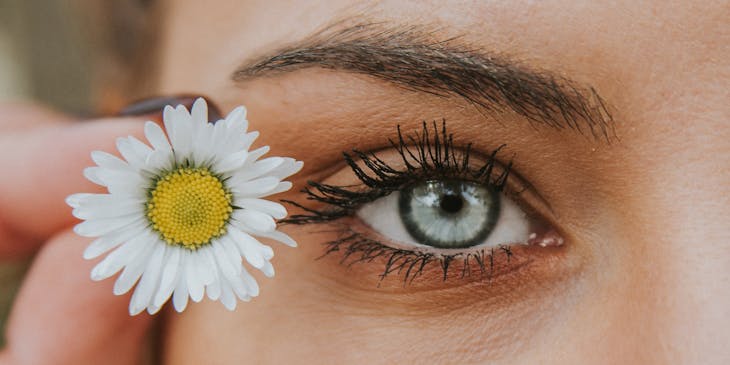 An eye-catching photo of a woman's eye next to a white and yellow flower.