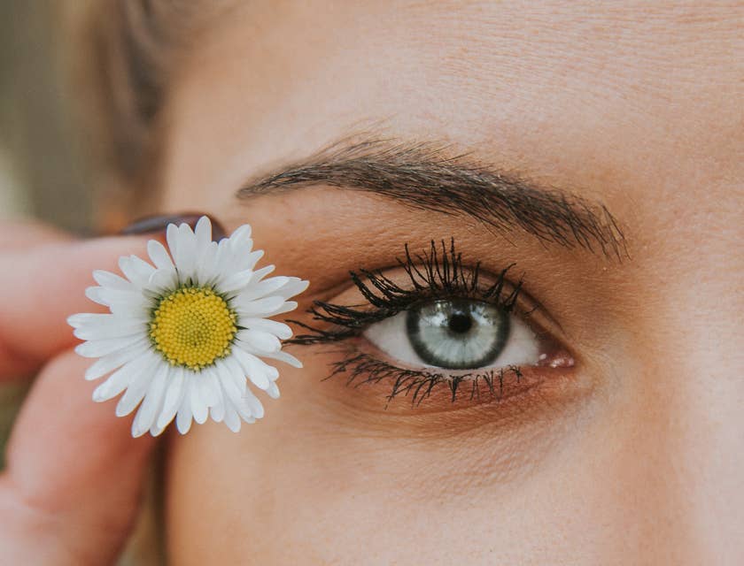 An eye-catching photo of a woman's eye next to a white and yellow flower.