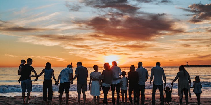 A large family standing together and facing the ocean at sunset.