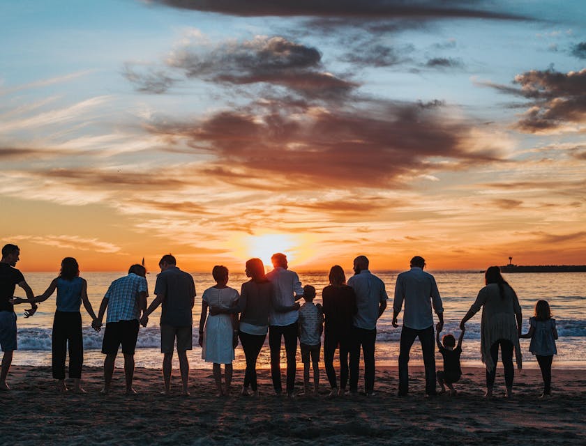 A large family standing together and facing the ocean at sunset.