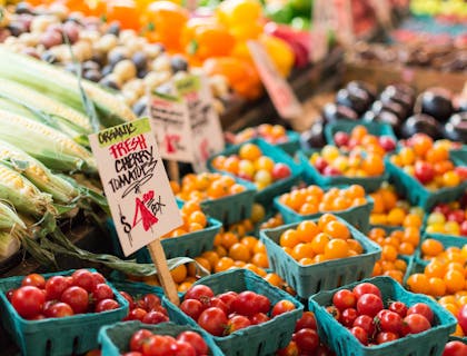 Körbe mit Tomaten, Mais und anderen Gemüsearten werden auf einem Bauernmarkt zum Verkauf angeboten.