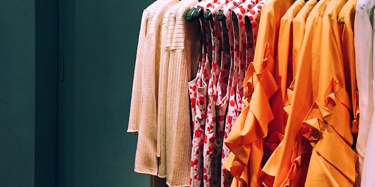 Rack of women's shirts and cardigans in a fashion store grouped by color and style.