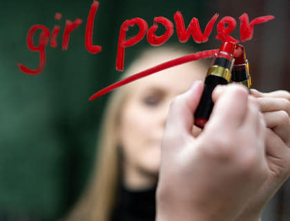 A female writing a message of empowerment with lipstick on a mirror.