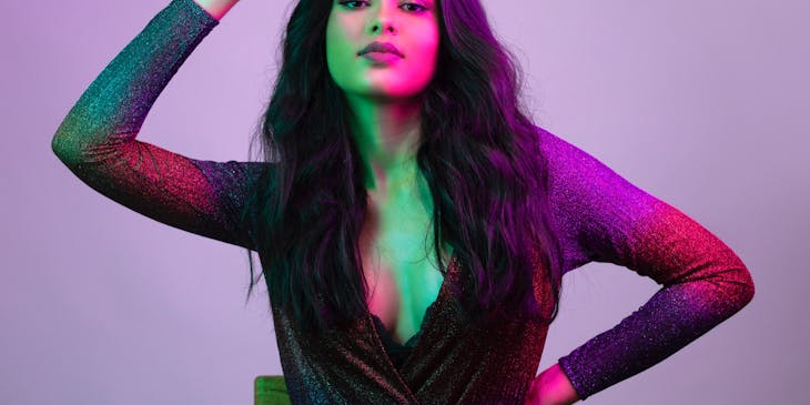 Woman in long sleeve top with long black hair against purple background.
