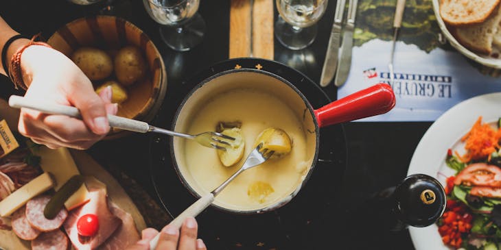Two people dipping food into a fondue pot.