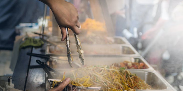 Una persona che lavora in uno stand gastronomico mentre mette del cibo in un contenitore di alluminio.